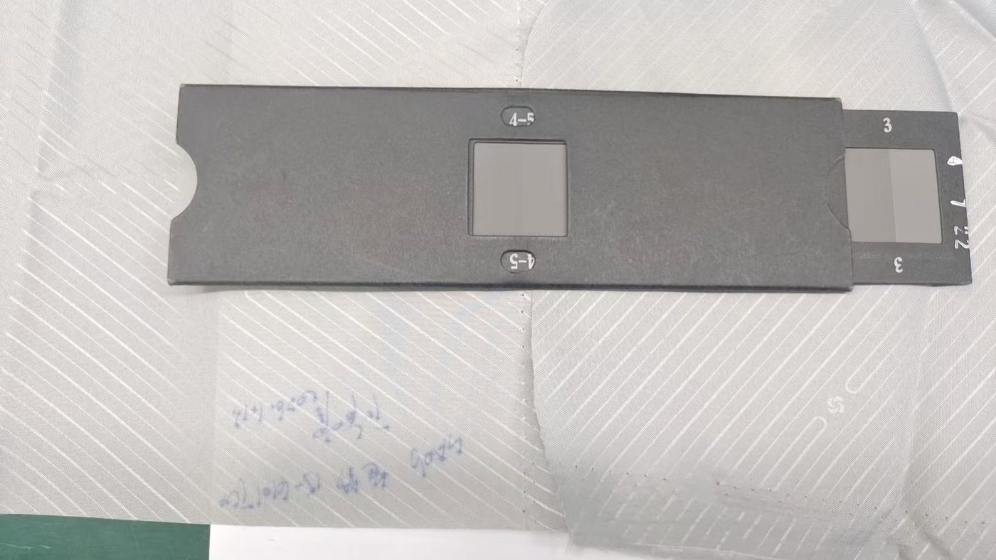 A grey scale card opened on a white woven fabric lot, with the grade 3-4 and grade 3 reference pairs visible in the card windows
