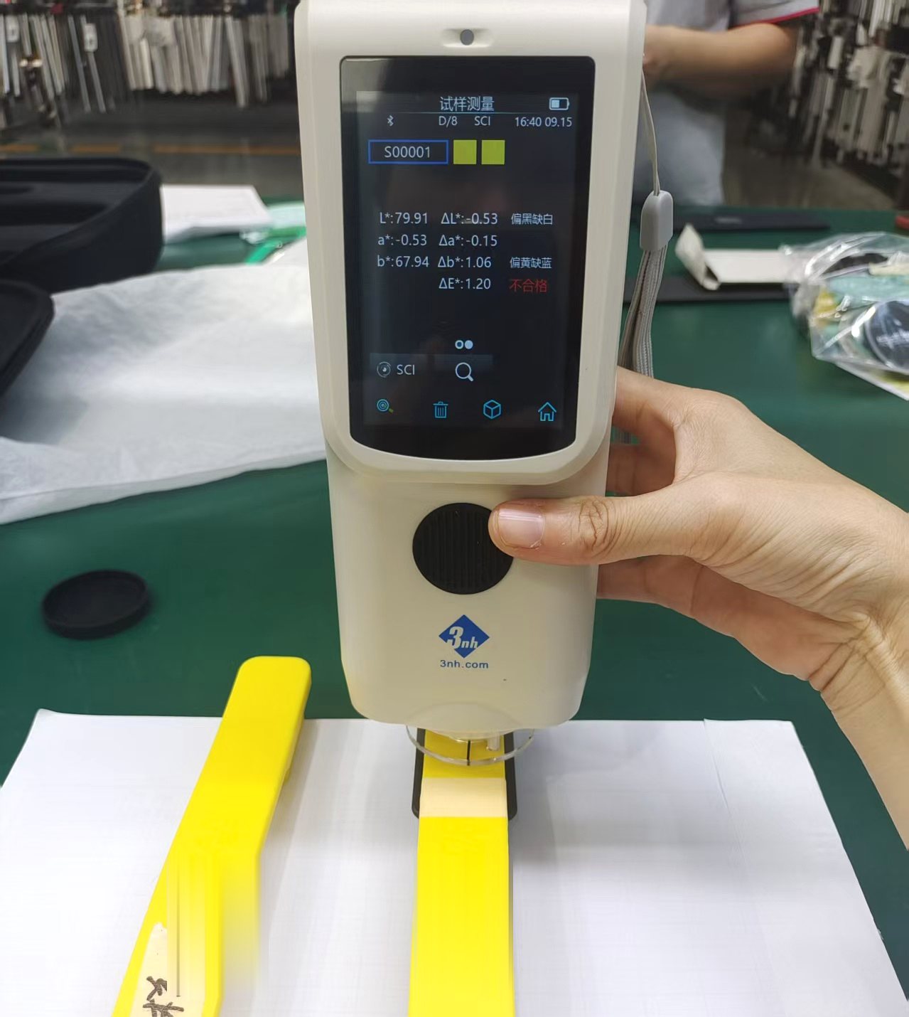 A colour-difference meter held over a yellow trolley tube, its screen reading ΔE 1.20 and marked as failing