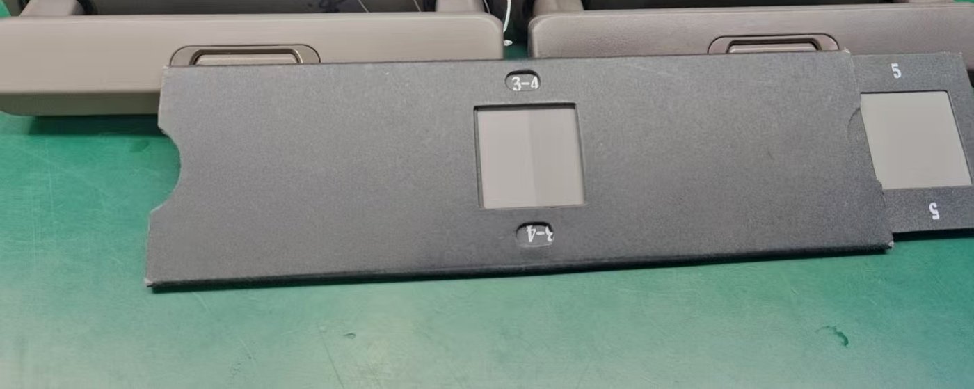 A grey scale reference card resting against a beige trolley handle component on a green workbench, with a second card visible at the right edge