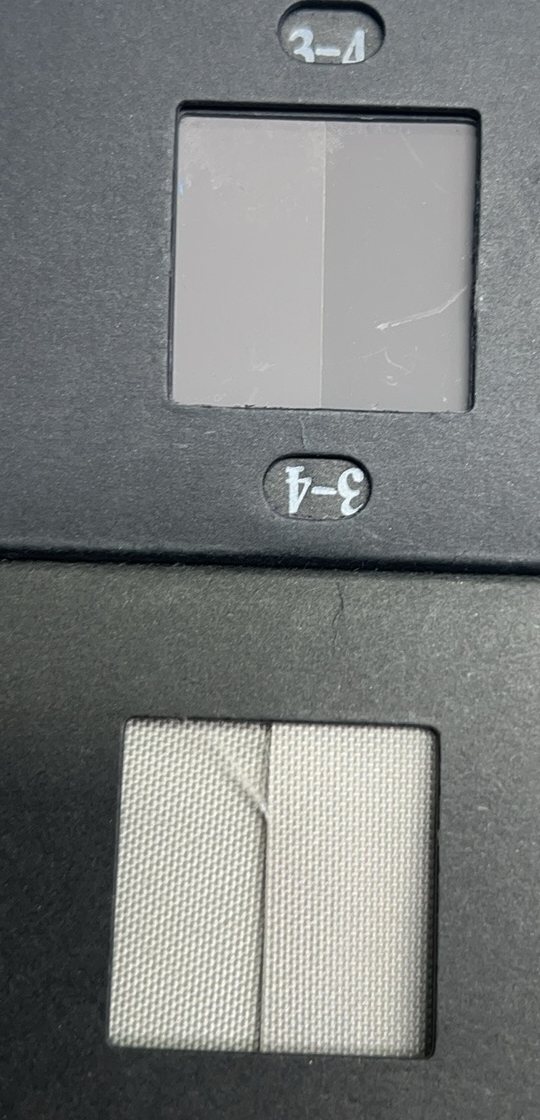 A grey scale card holding a grade 3-4 reference pair in its upper window and a white woven fabric sample pair in its lower window